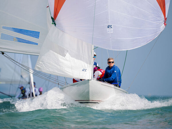 A Dragon drives through a wave under spinnaker.